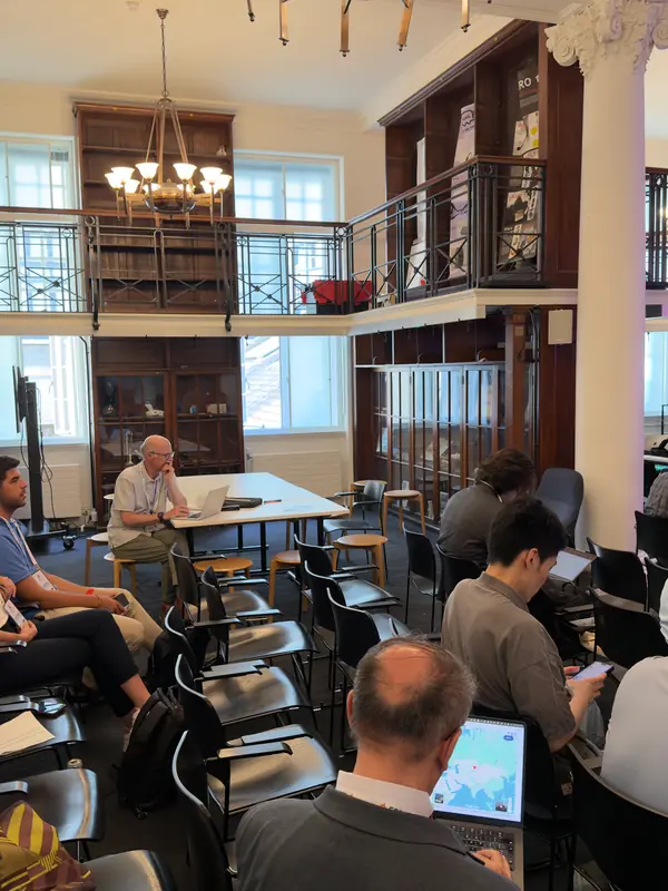 Participants seated in a galleried hall with bookshelves during a session.