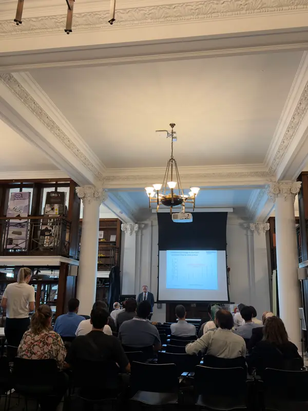 A session at ECRES 2026 in London: the audience faces the screen between white columns, under a chandelier.