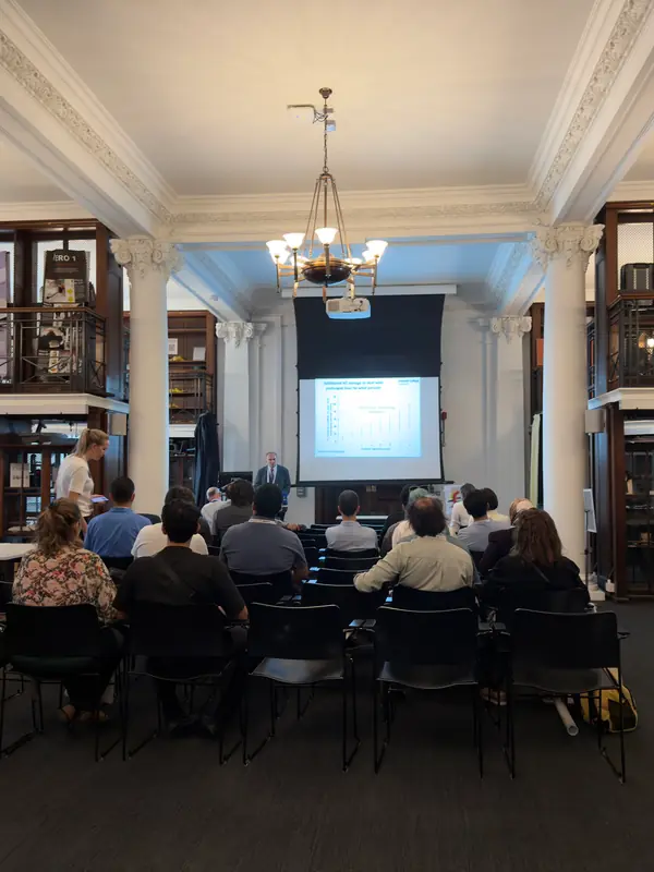 Wide view of the session hall with galleries of bookshelves and a full audience.